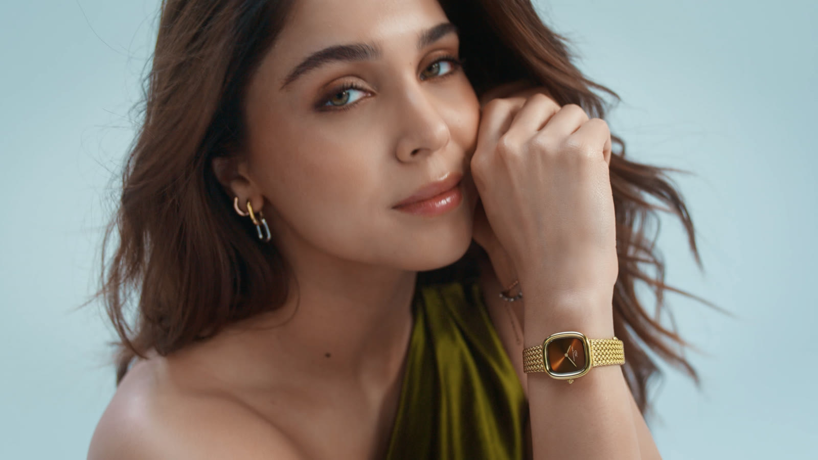 Close portrait with a gold watch on a soft blue backdrop