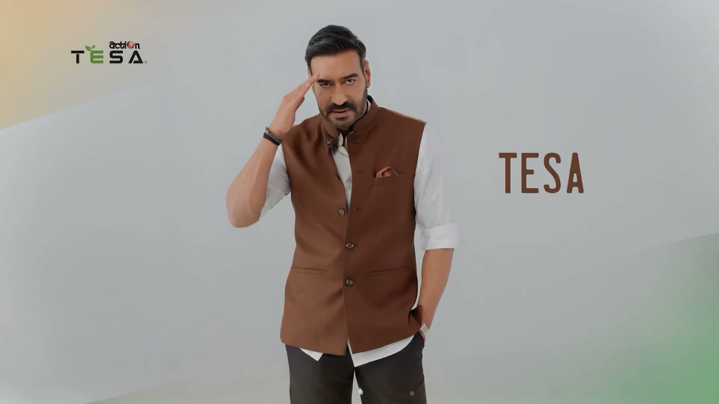 A man in a brown waistcoat gestures near his head against a plain white studio backdrop, beside the TESA logo